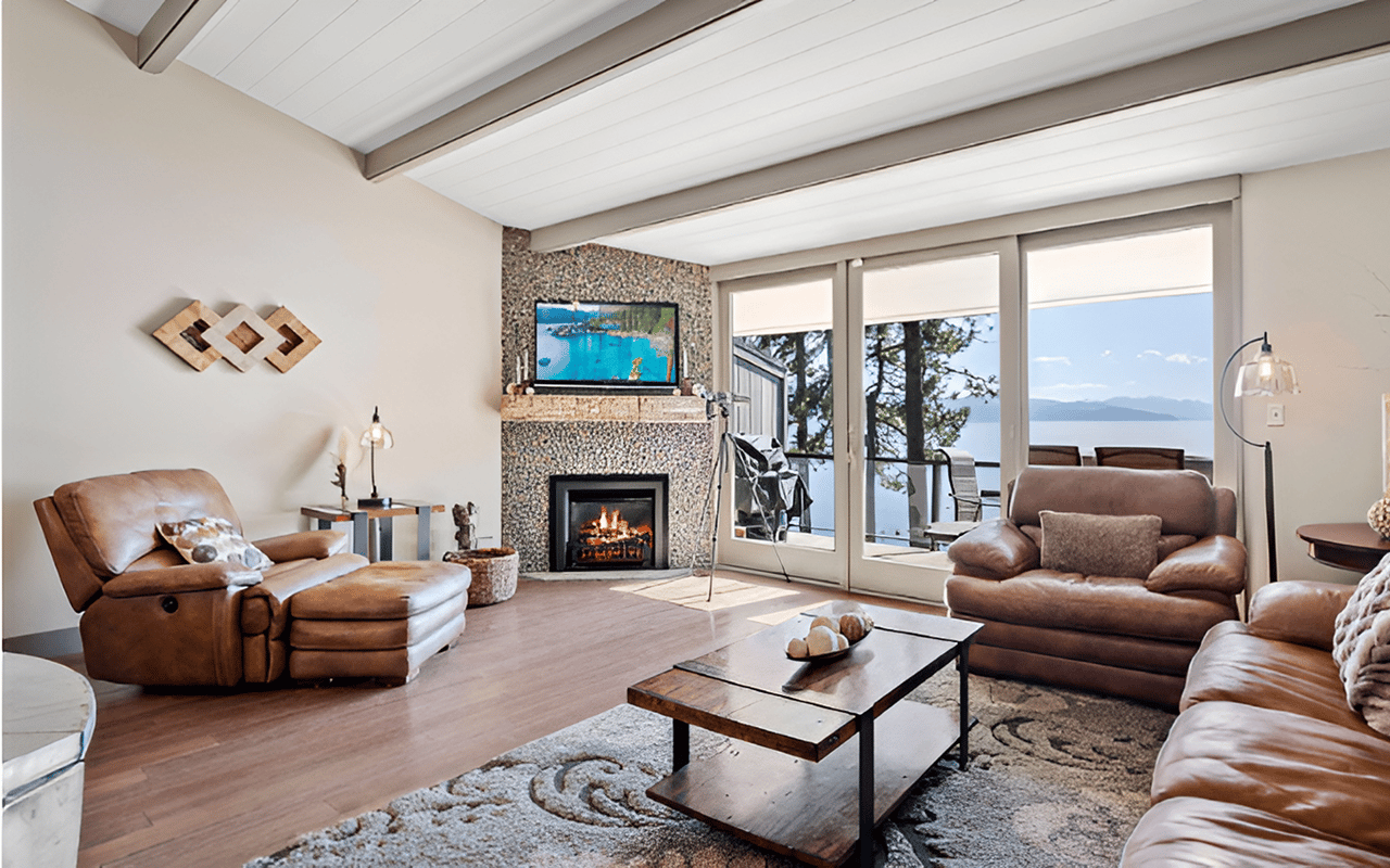 Living room with a stone fireplace and leather seating overlooking a lake and mountains.