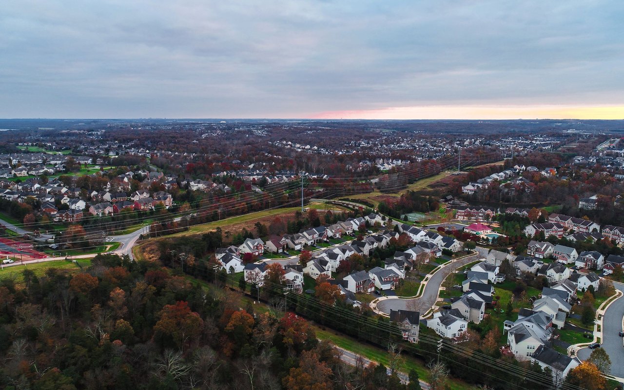 Aerial view of a suburban neighborhood with winding streets and autumn trees beneath a cloudy evening sky.