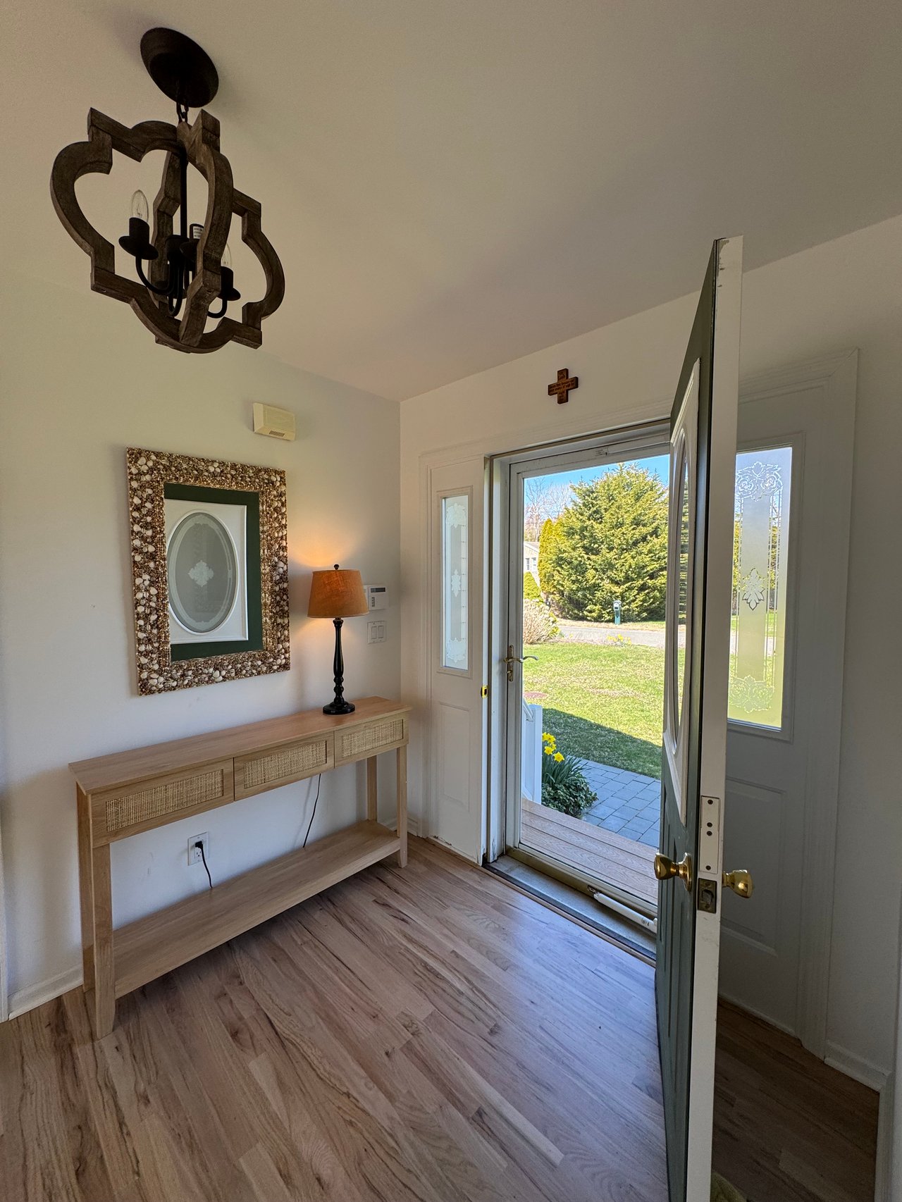 Entry foyer with a wood console table and open front door overlooking a lawn and daffodils.