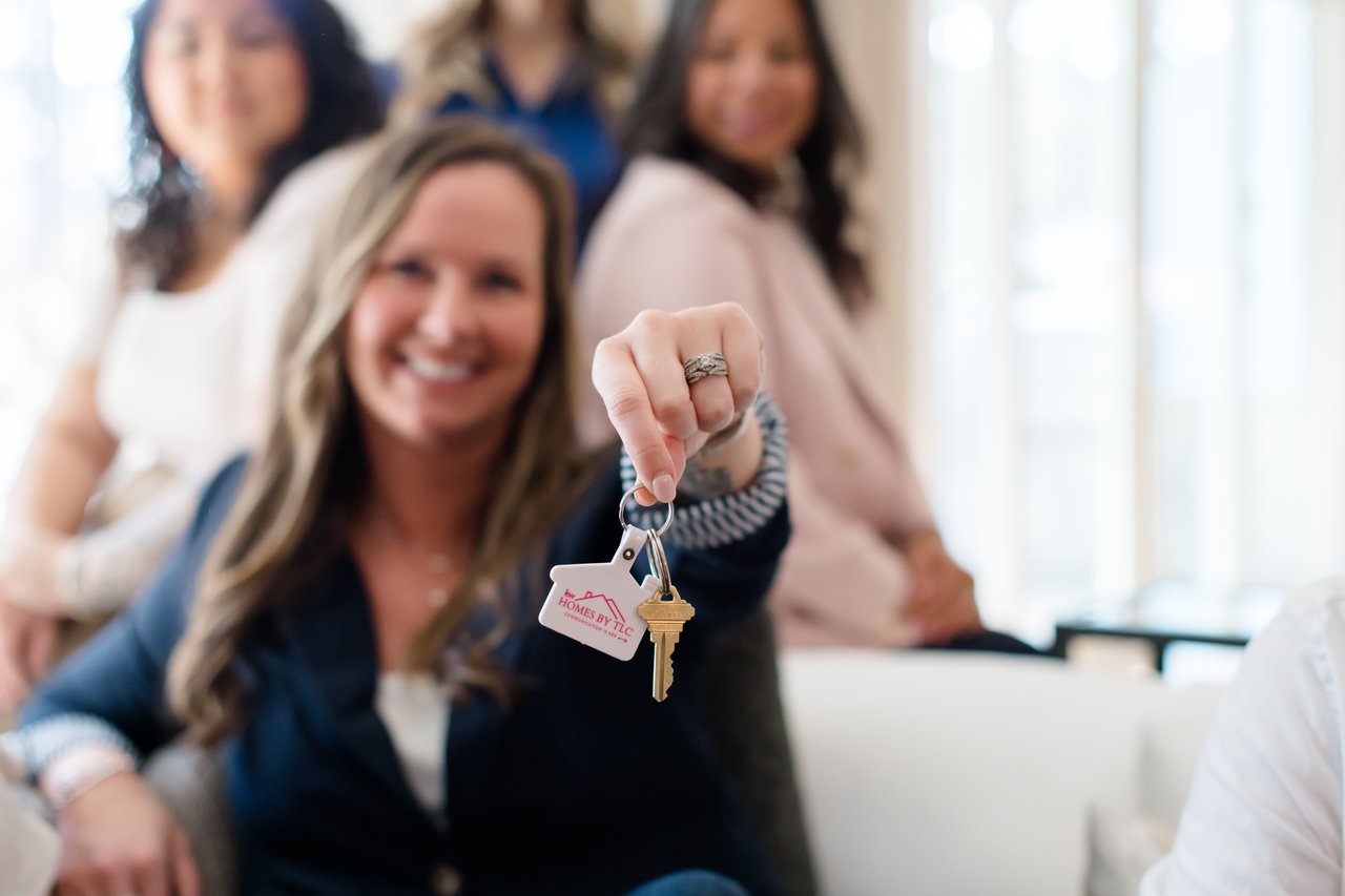 A woman holds up house keys with three smiling women behind her.