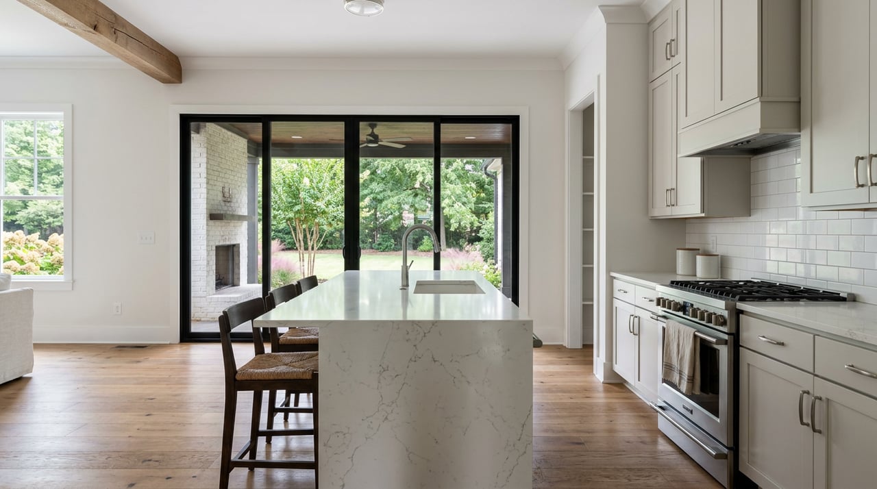 White kitchen with quartz island, stainless range, and black-framed glass doors opening onto a covered porch.