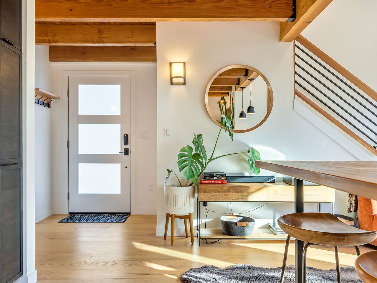 Bright entryway with exposed wood beams, a round mirror, and a staircase with black railings.