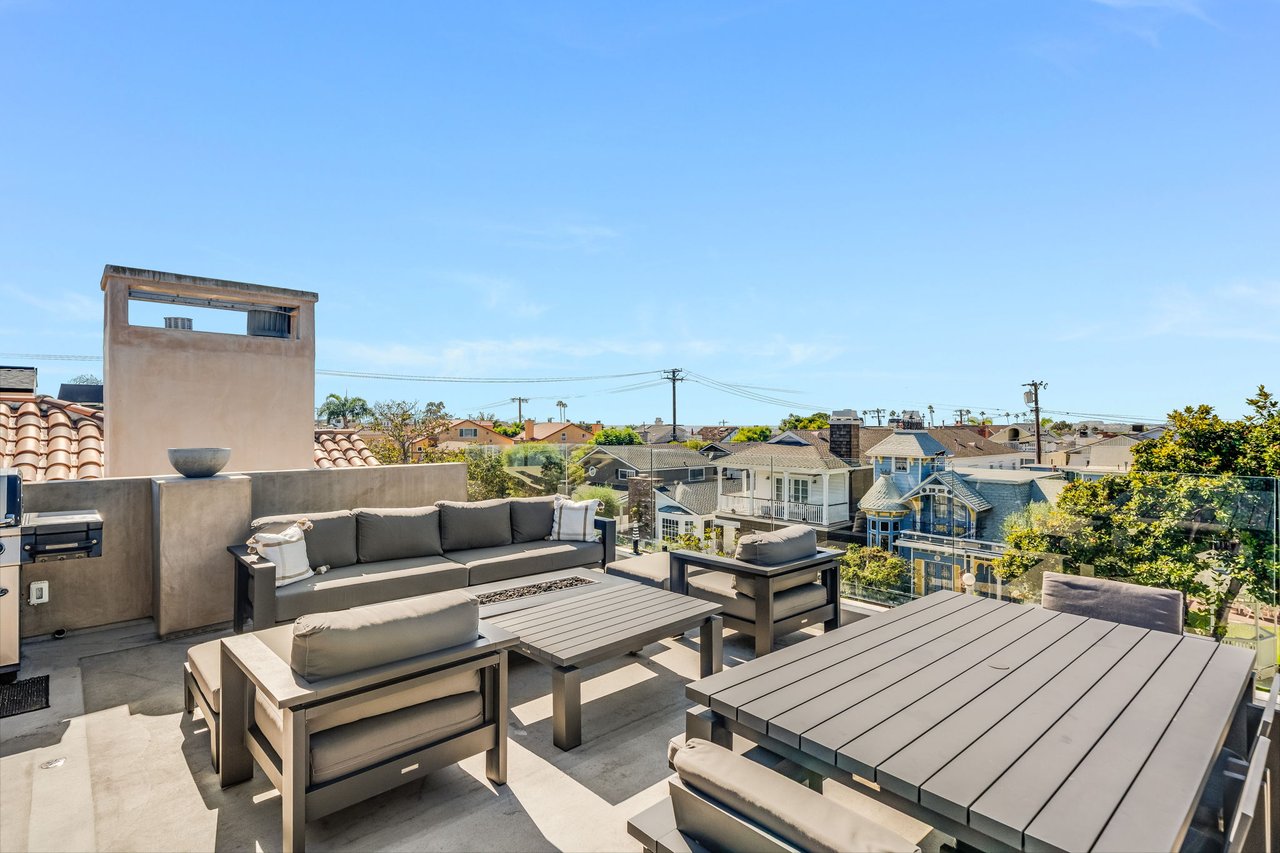 Furnished rooftop terrace with gray seating, a dining table, and views over nearby homes.