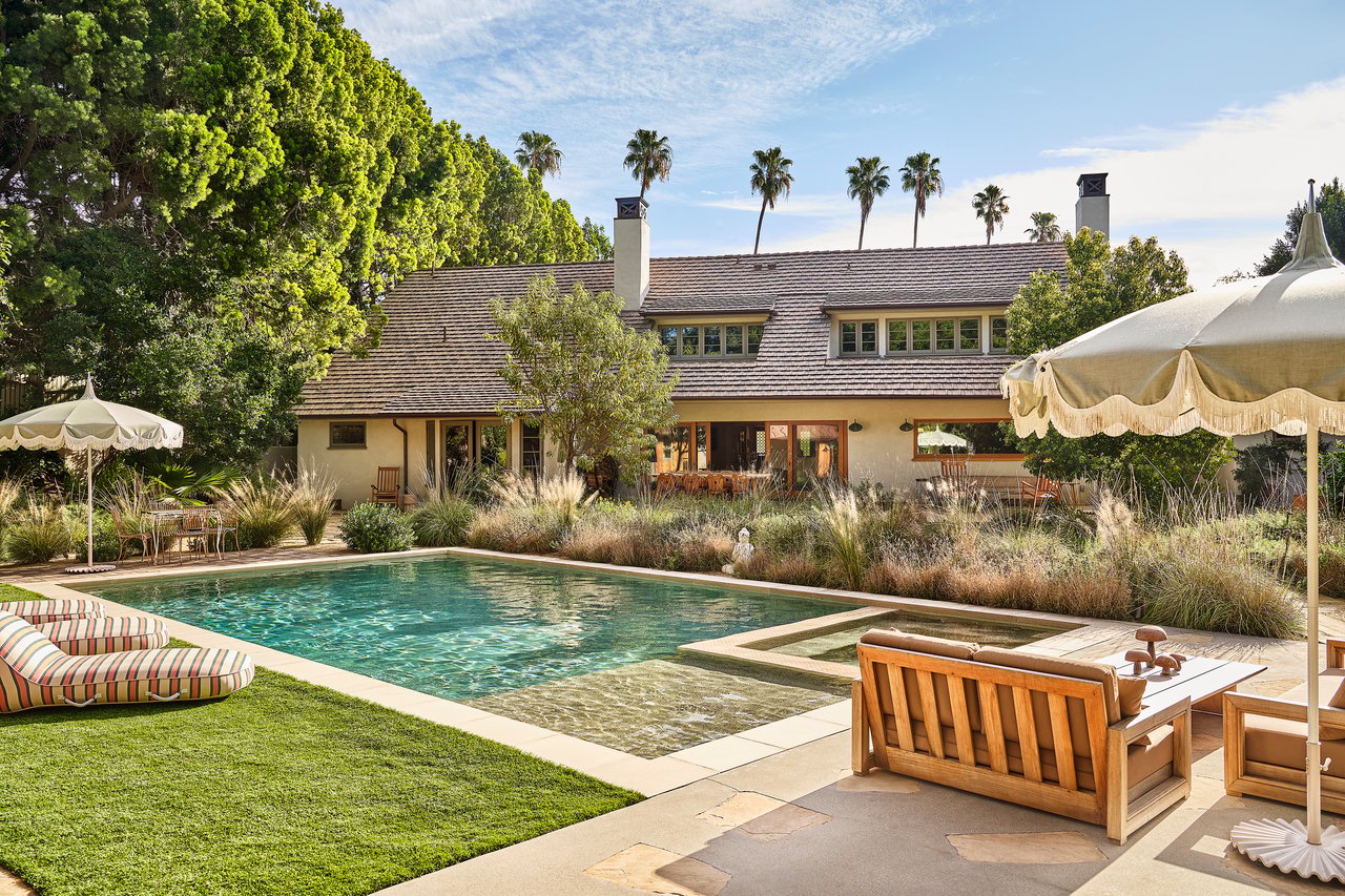 Home with a landscaped pool, shaded patio seating, and palm trees.