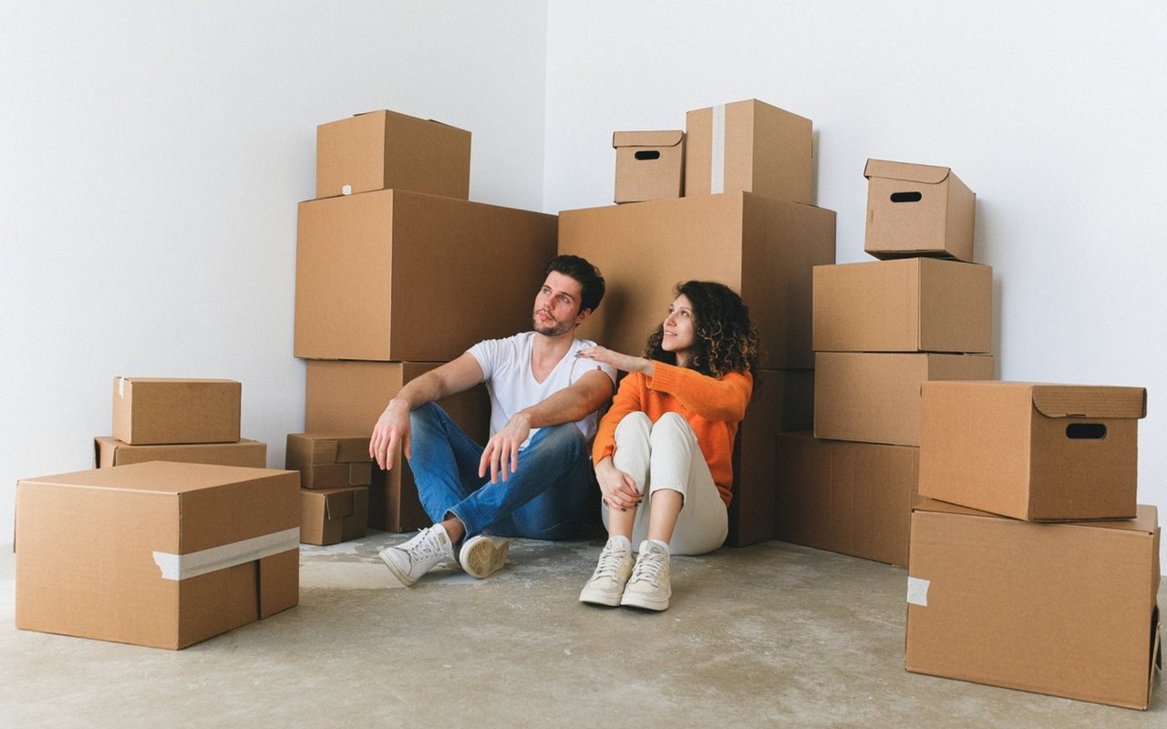 Couple sitting among moving boxes in a mostly empty room