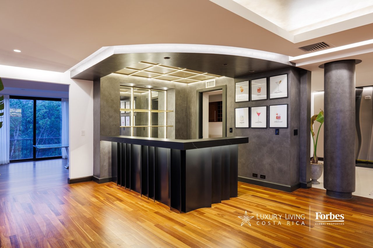 Penthouse bar area with a black counter, illuminated shelving, and wood flooring.