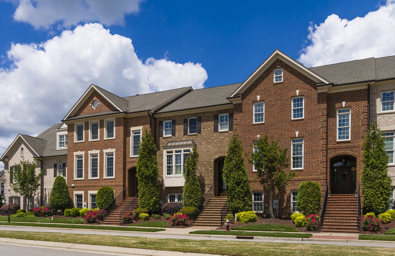 Attached brick townhouses with front steps and landscaped gardens along the sidewalk.