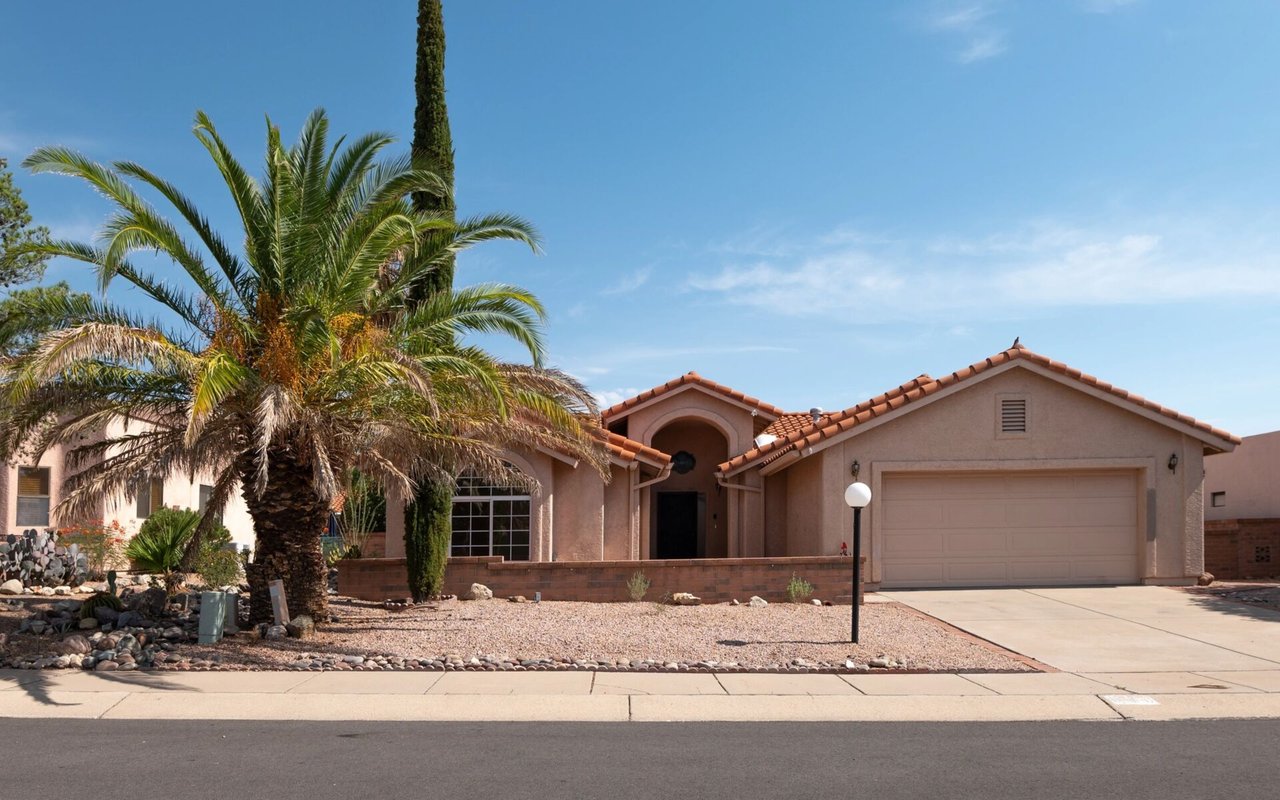 Single-story stucco home with a tile roof, two-car garage, palm trees, and desert landscaping.