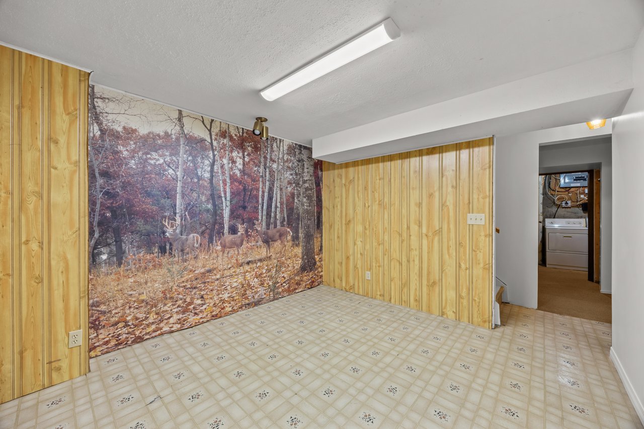 Basement room with wood paneling, a forest mural, patterned tile flooring, and laundry area doorway.