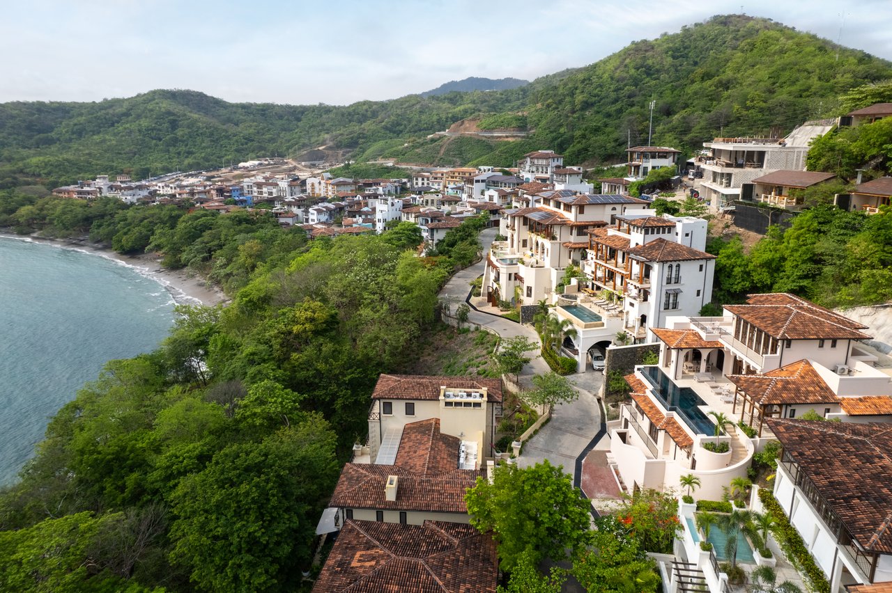 Aerial view of Las Catalinas homes along a green hillside above the ocean and curved shoreline.