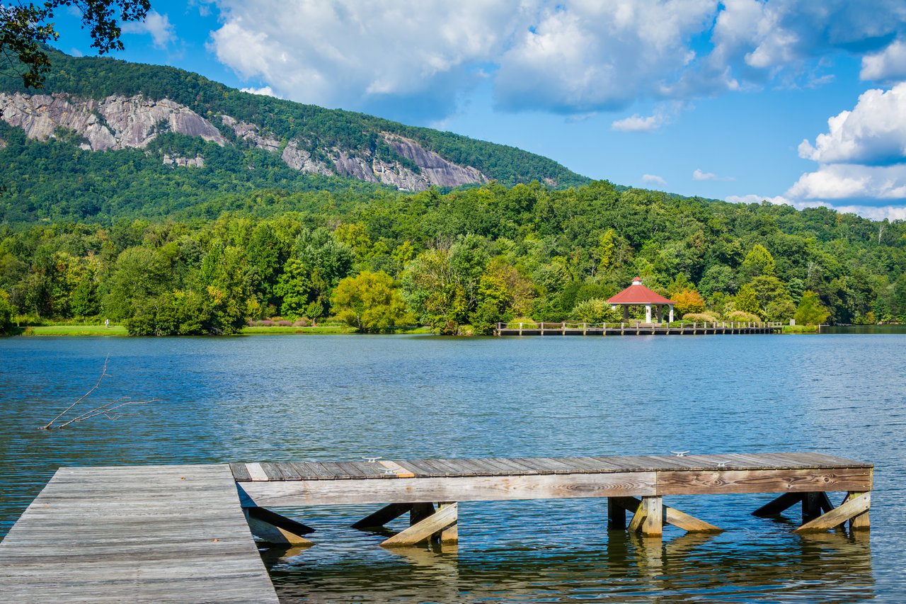 Lake with a wooden dock, red-roofed pavilion, and forested mountain with exposed rock.