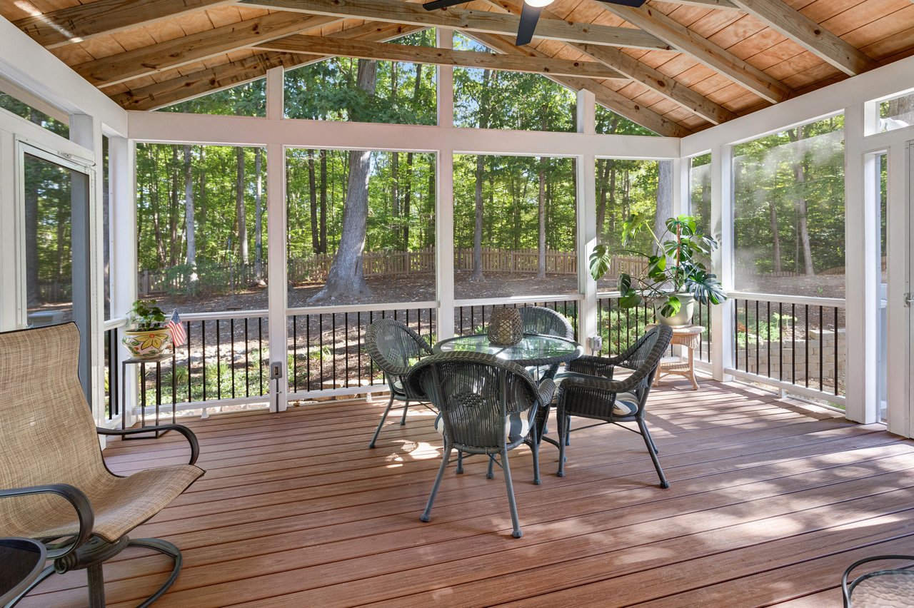 Screened porch with a vaulted wood ceiling, wicker dining set, and wooded views.