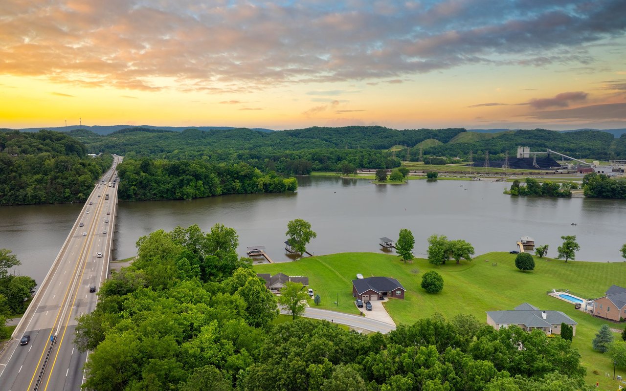 Bluff City riverfront at sunset, with a highway bridge, wooded hills, and homes.