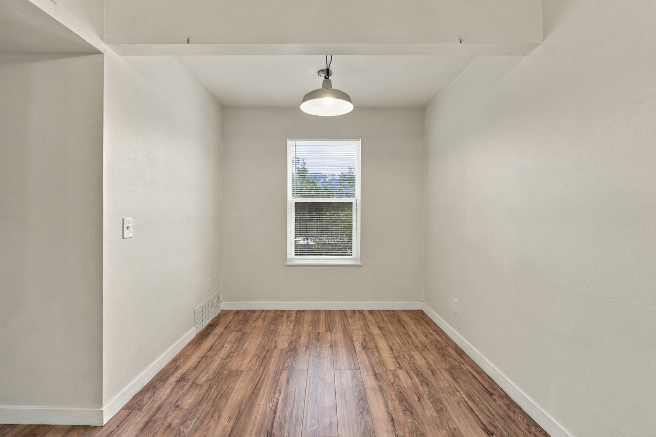 Vacant room with wood-look flooring, a window with blinds, and a hanging ceiling light.