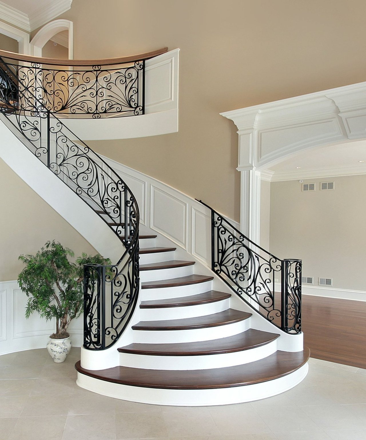 Curved staircase with dark wood treads and ornate black iron railings.