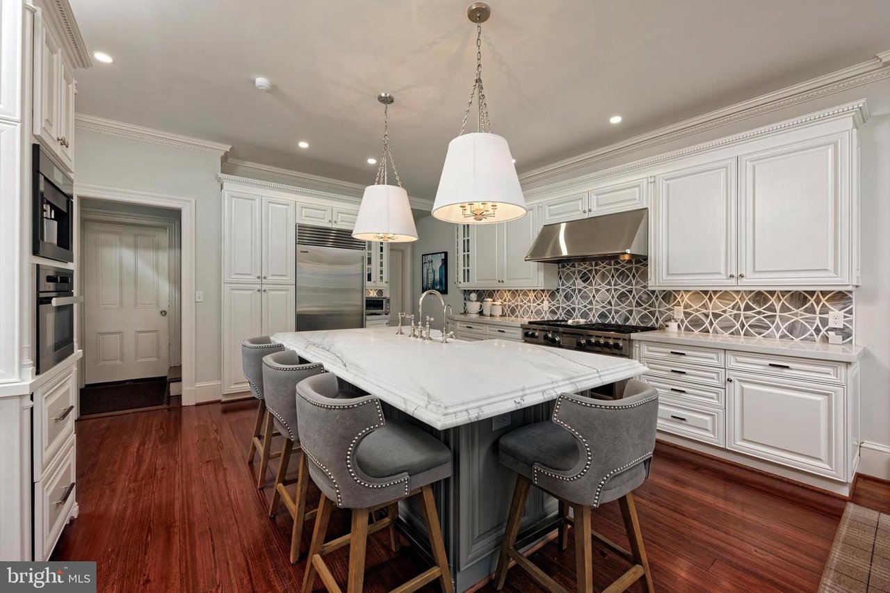 Kitchen with a marble island, gray bar stools, white cabinetry, and a geometric tile backsplash.