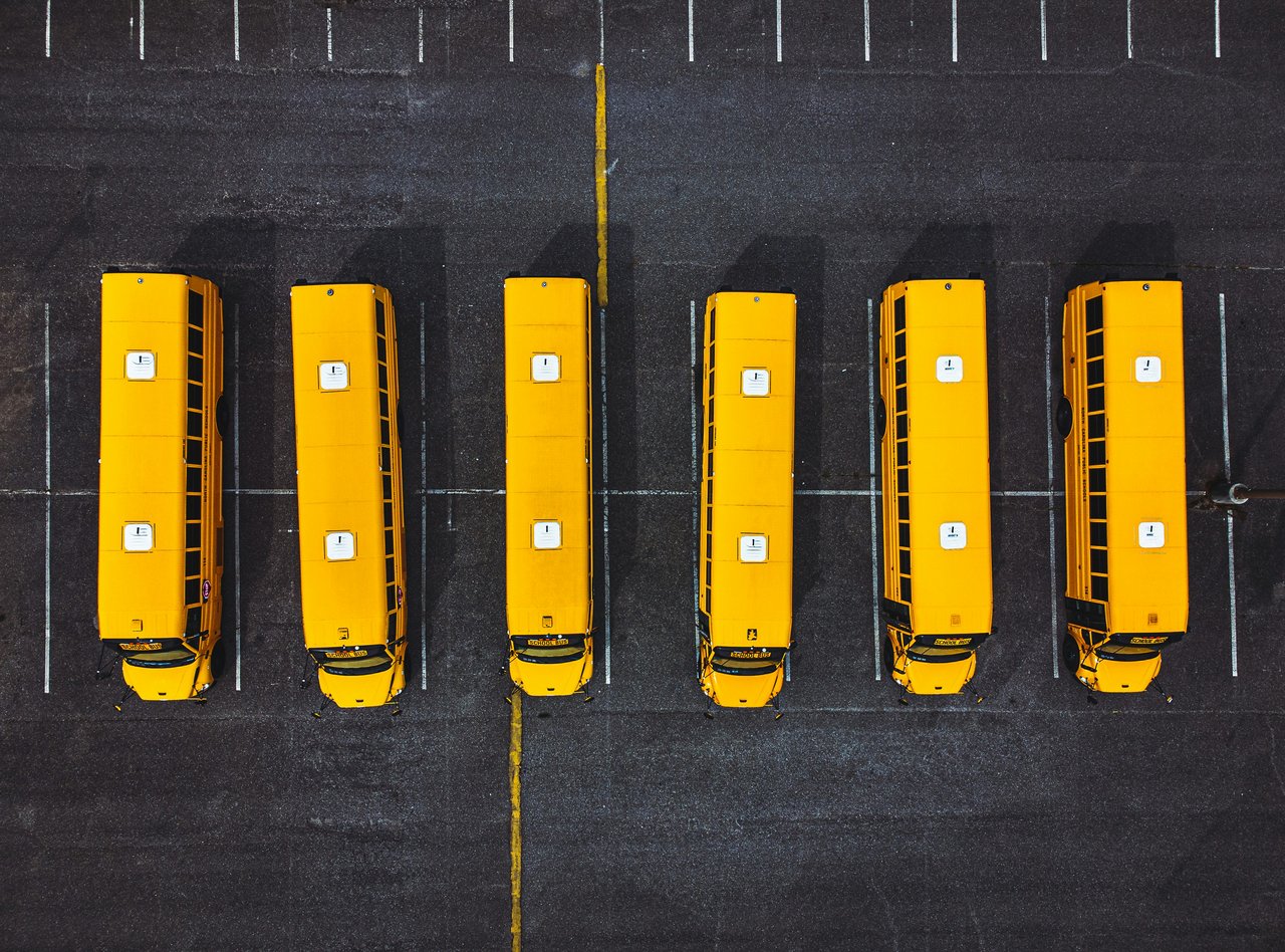 Aerial view of six yellow school buses parked in rows at a transportation depot facility