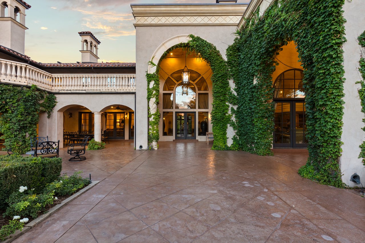 Estate courtyard with ivy-covered arches, a stone balcony, and wrought-iron benches.