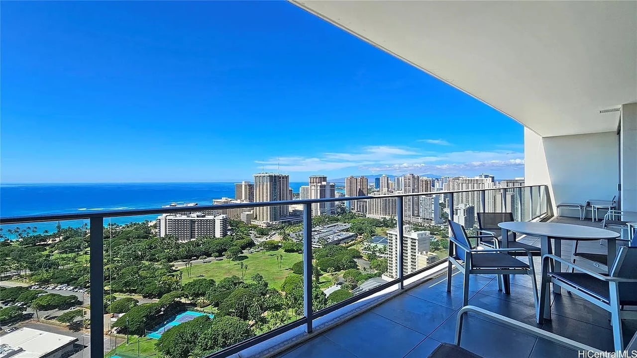 Condo balcony overlooking the Pacific Ocean and Waikiki skyline, with outdoor dining furniture.