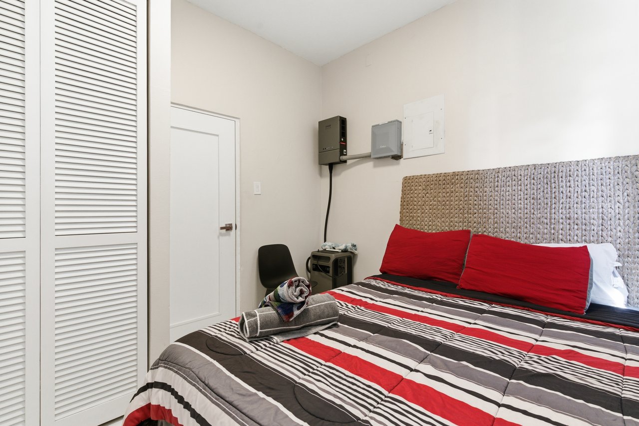 Furnished bedroom with a striped comforter, woven headboard, and louvered closet doors.