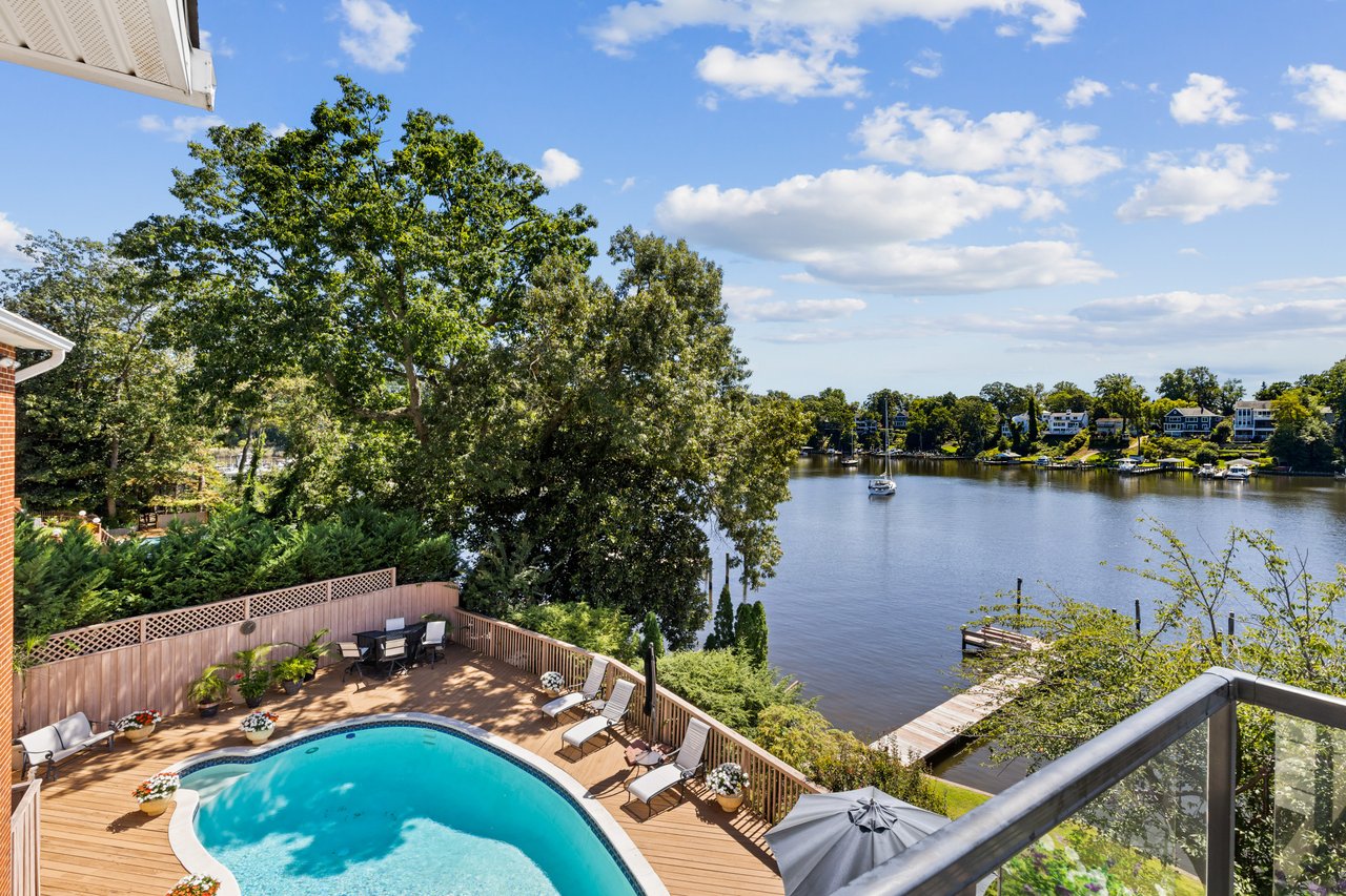 Backyard pool and furnished deck overlooking a river, with a dock and sailboat.