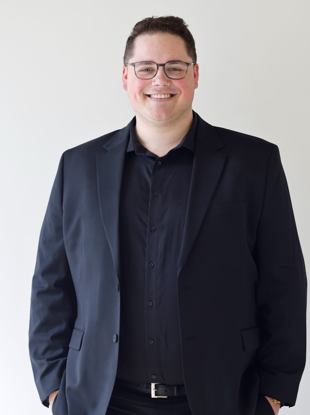 Jordan McKay smiling in glasses and a dark suit jacket.