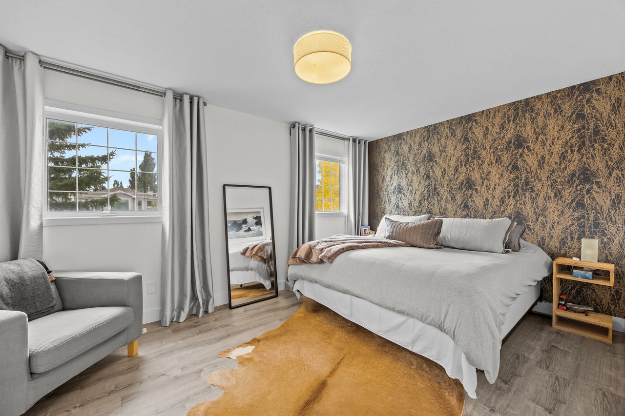 Bedroom with a large bed, botanical-patterned accent wall, two bright windows, and tan hide rug.
