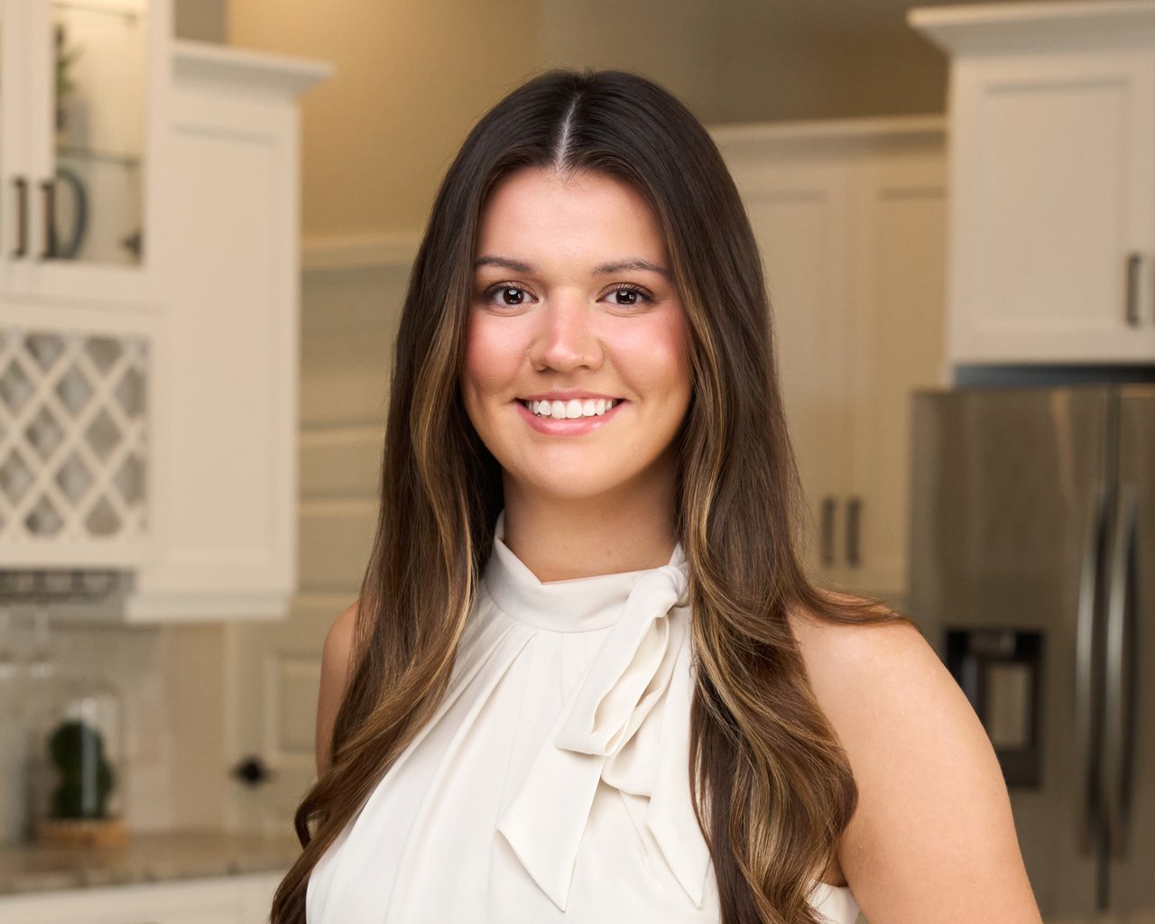 Madison Bird smiling in a white blouse in a kitchen.