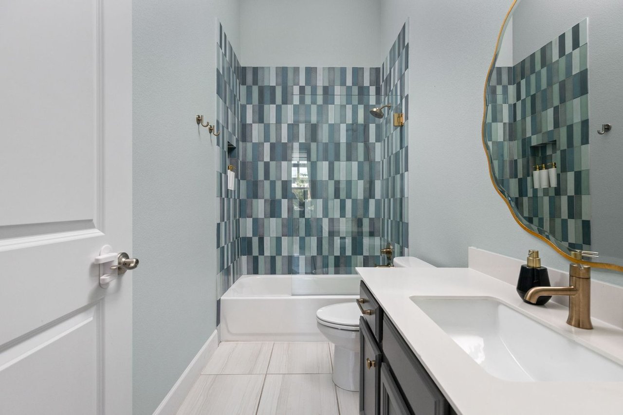 Bathroom with a blue-and-gray tiled tub and shower, dark vanity, and gold-framed mirror.