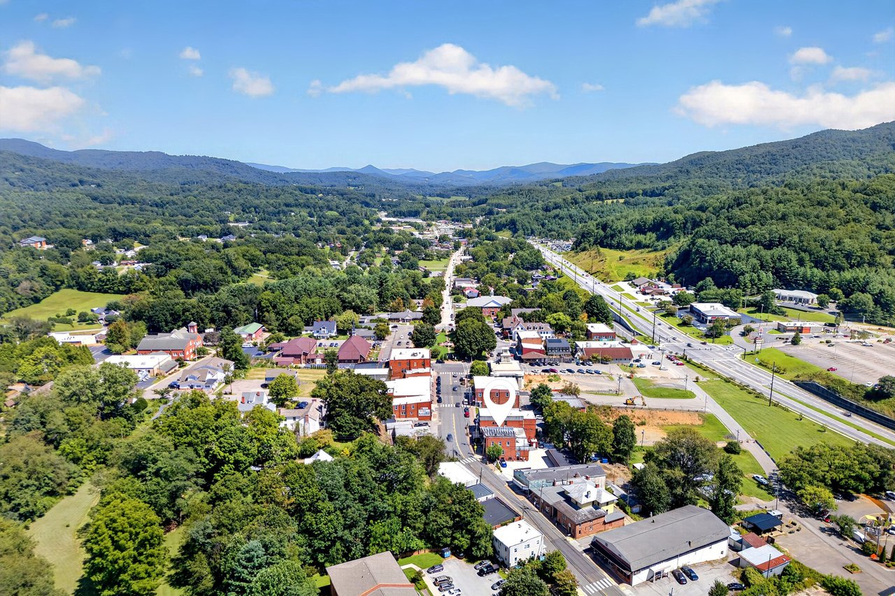 Aerial view of a downtown commercial building marked among shops, a highway, and wooded mountain ridges.
