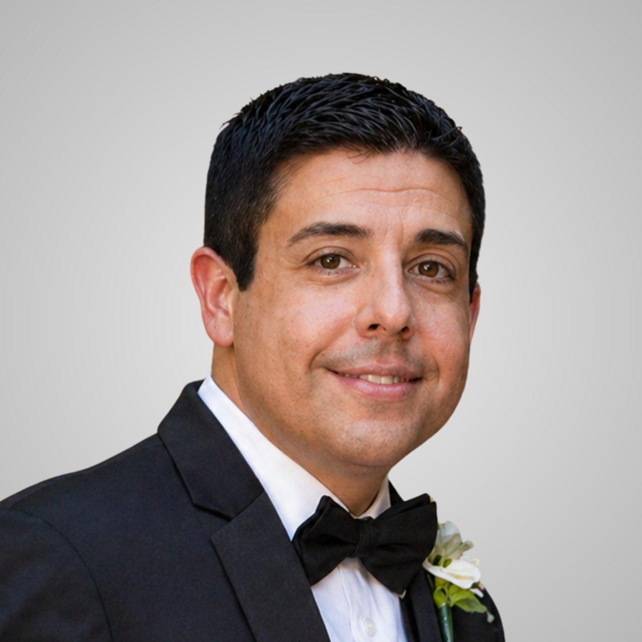 Luis Carrera in a black tuxedo and bow tie with a white boutonniere.