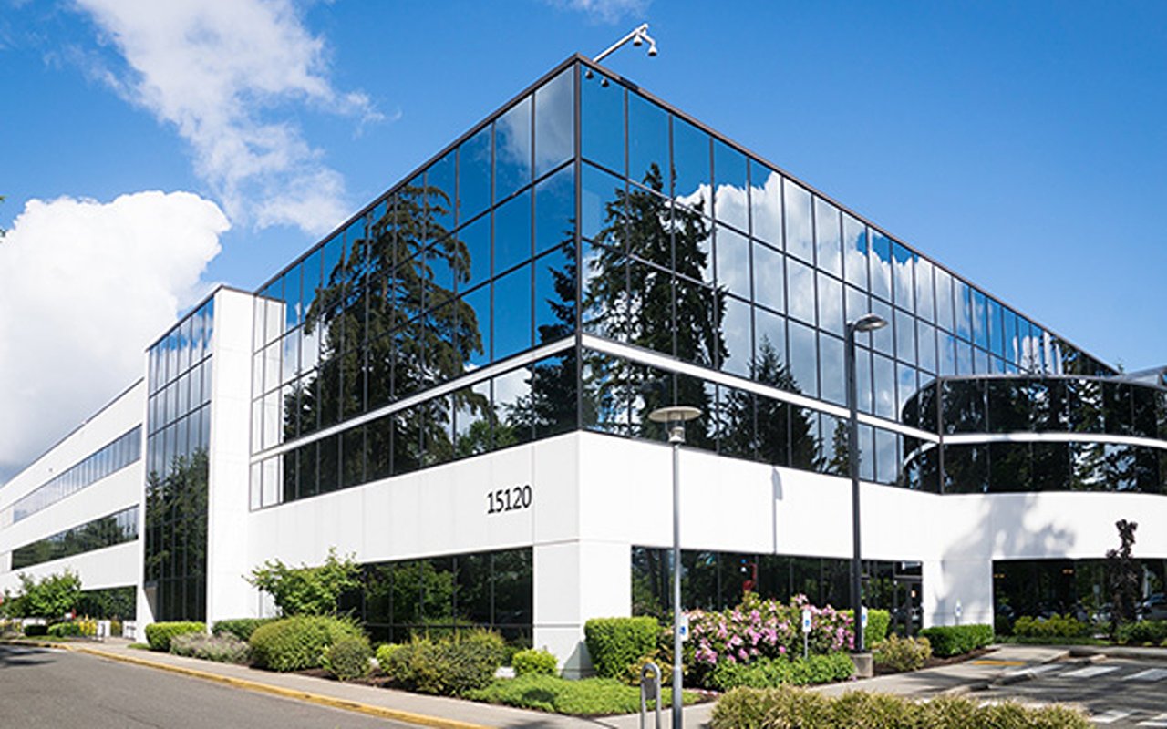 Modern office building with reflective glass windows, white facade, and landscaped entrance.