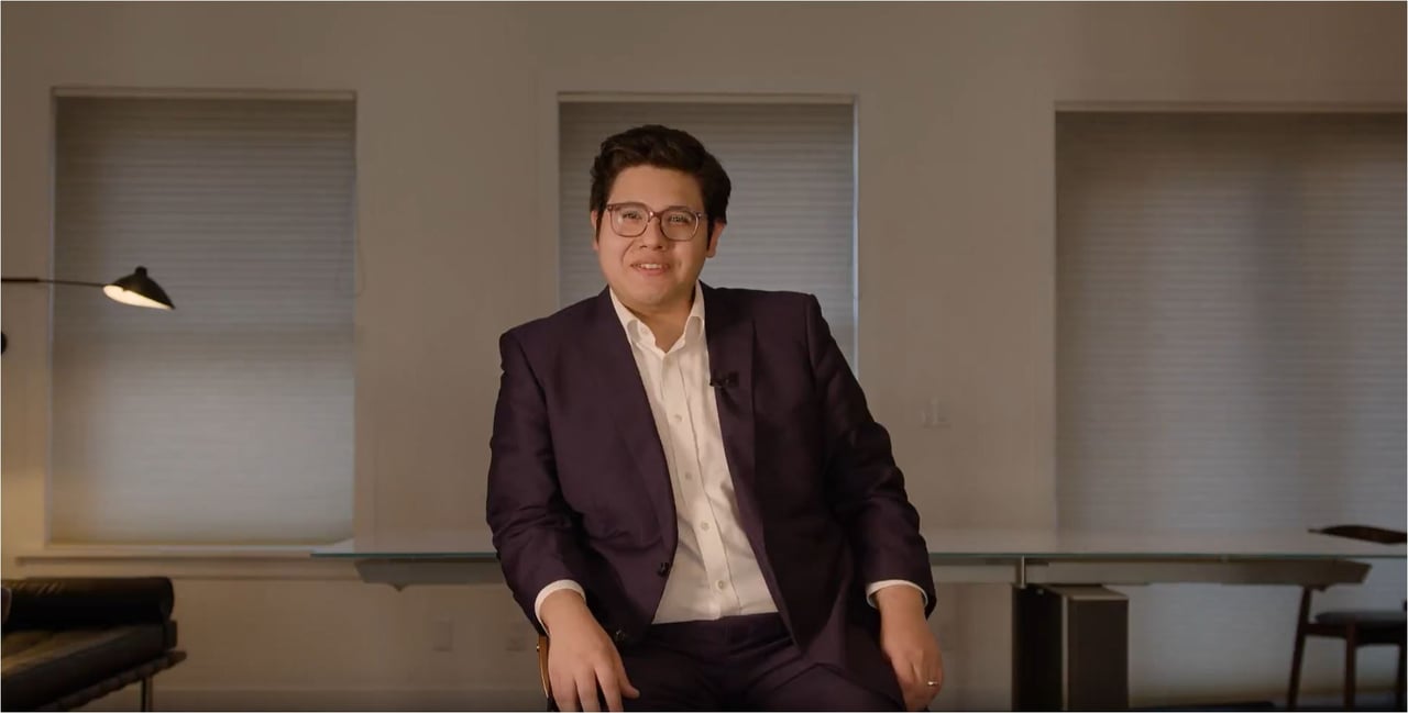 David Lozada seated in a dark suit and glasses in a modern office.
