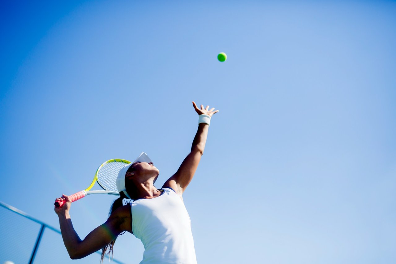 Tennis player preparing to serve beneath a clear blue sky.