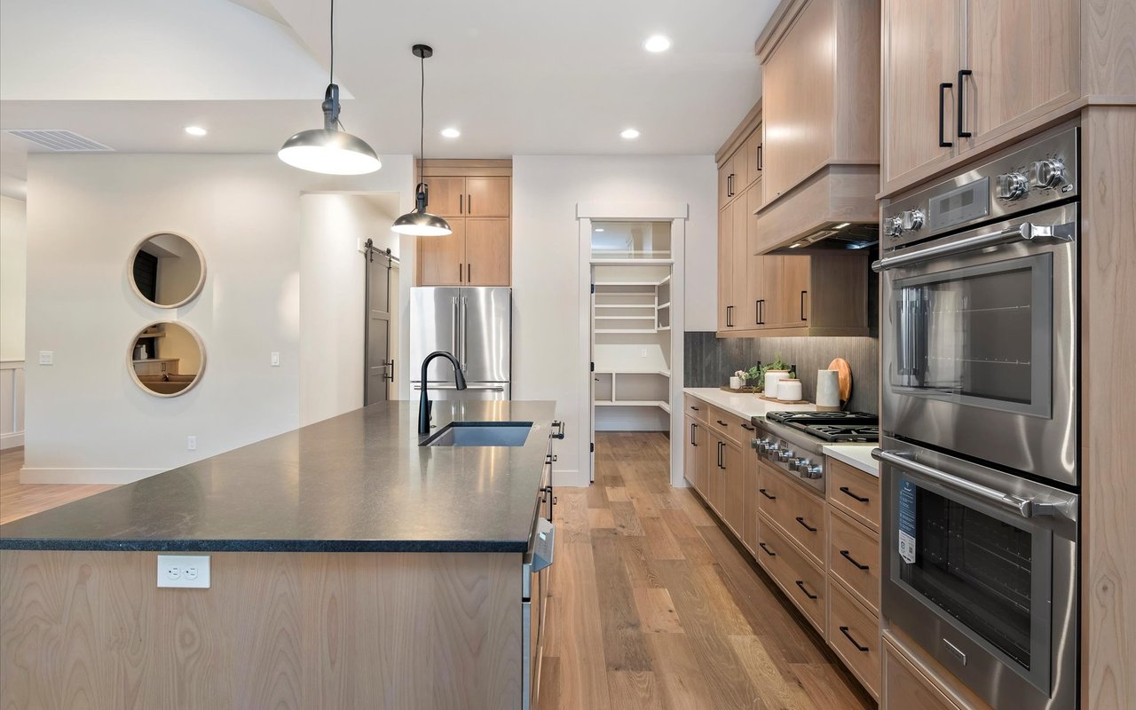 Gourmet kitchen with double wall ovens, dark counter-top on island, and pantry