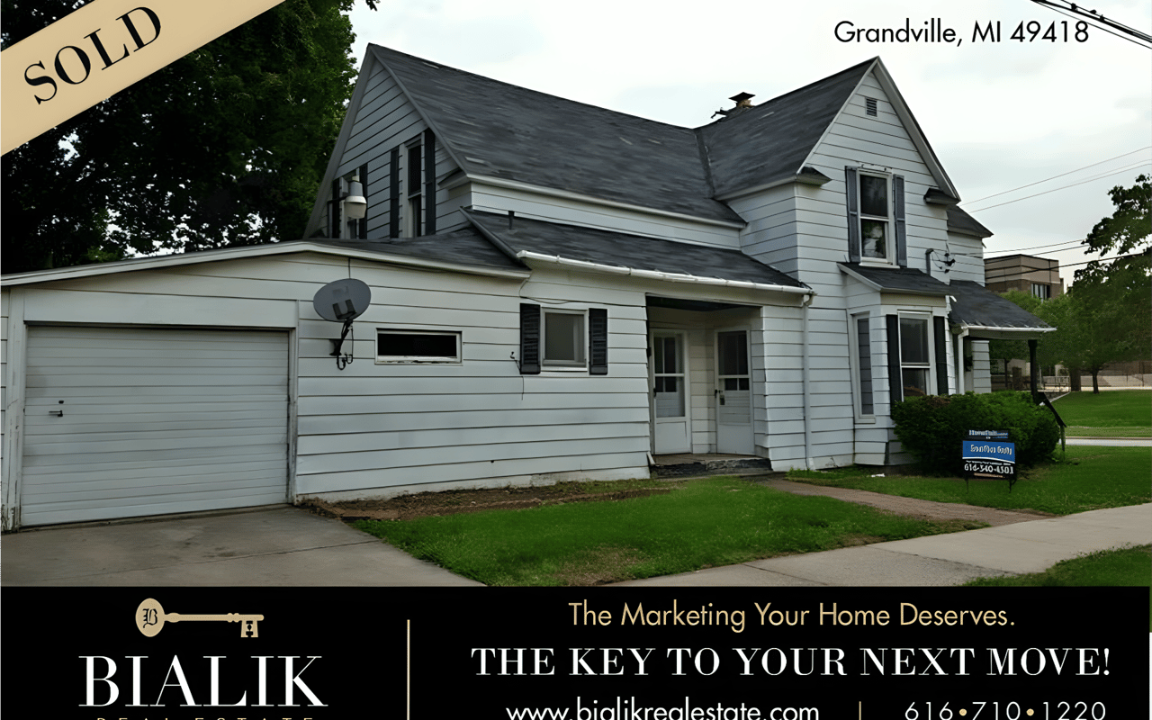 White two-story house with attached garage and lawn, marked sold in Grandville, Michigan.