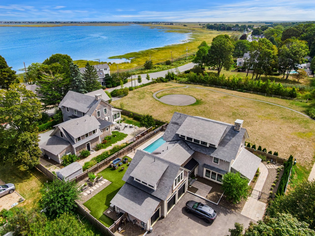 Aerial view of a gray-shingled home with a pool beside a coastal marsh and waterway.