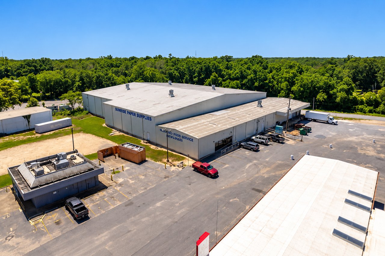 Aerial view of a large warehouse with loading areas and trucks, surrounded by woodland.