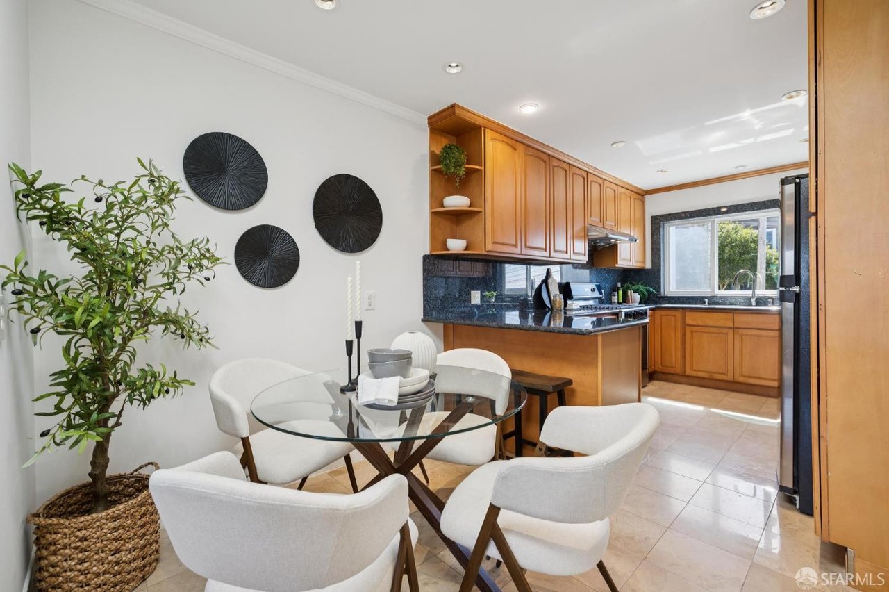 Kitchen and dining area with warm wood cabinets, dark counters, and a glass table with white chairs.