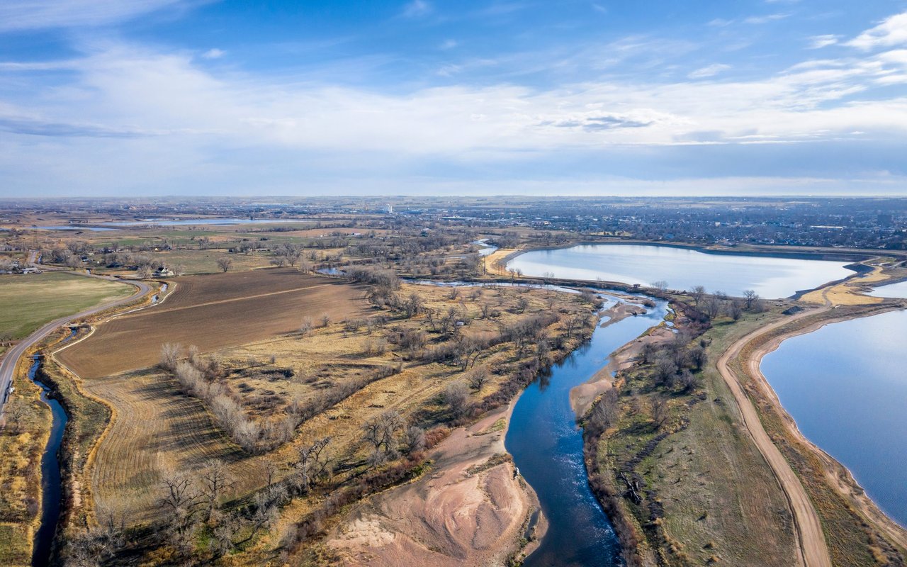 A river curves through open fields and wetlands beside a reservoir and distant town.