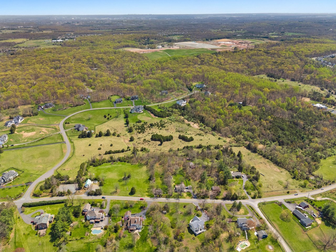 Aerial view of homes and open acreage bordered by spring woodland and winding roads.
