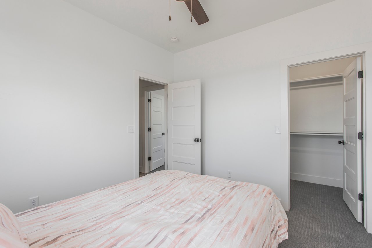 Bedroom with a pink-and-white striped quilt and an open closet.