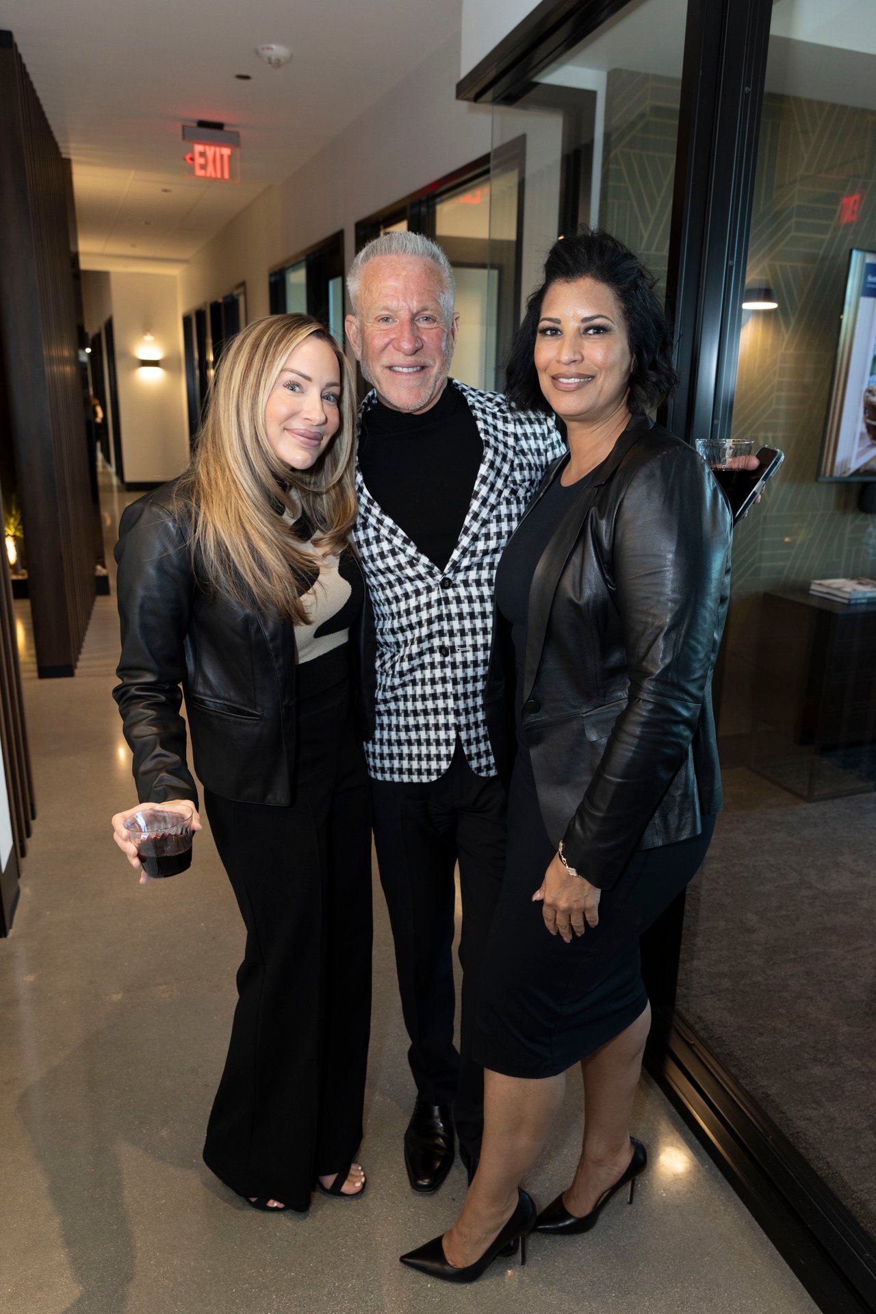 Three adults pose together in an office hallway; the man in the center wears a black-and-white patterned jacket.