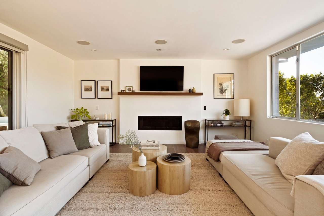 Staged living room with cream sofas, a fireplace, and a wall-mounted television.