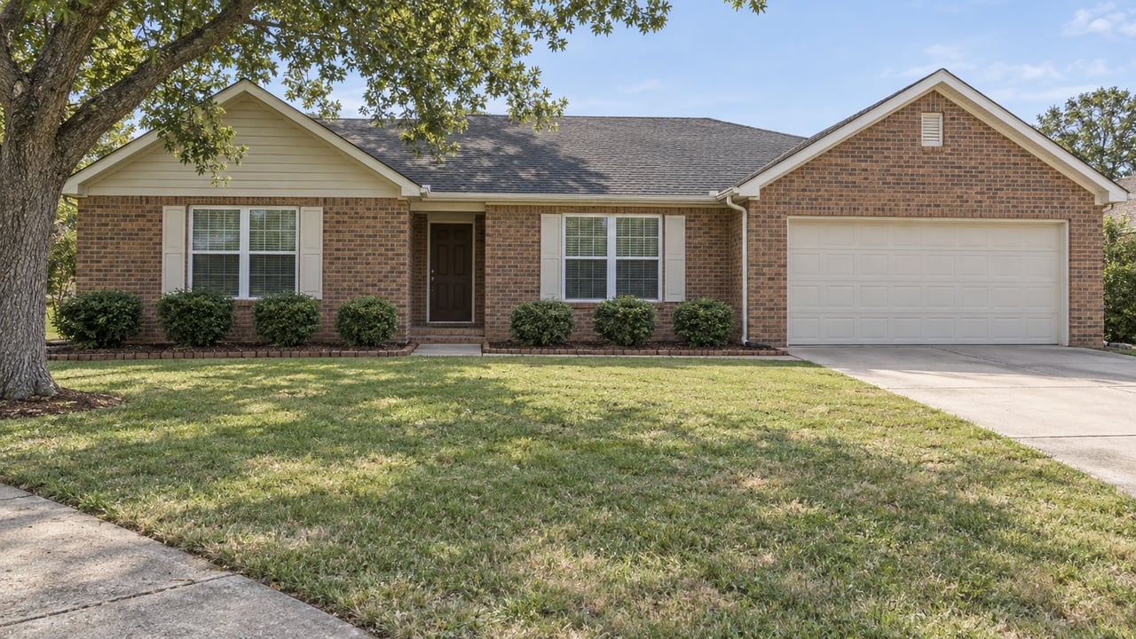 A single-story brick home with cream gables, an attached garage and an open lawn beneath a mature white oak.