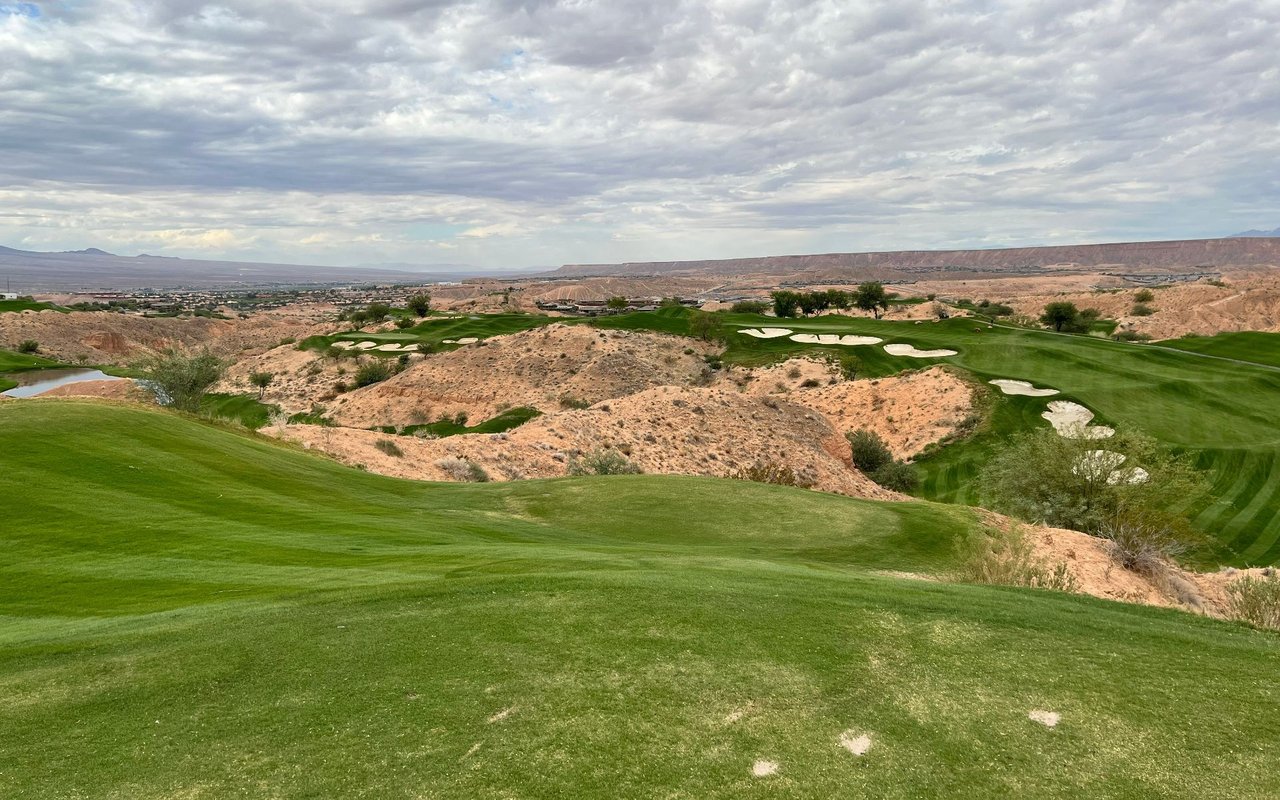 Somersett golf course winds through rugged terrain, with sand bunkers and distant homes.