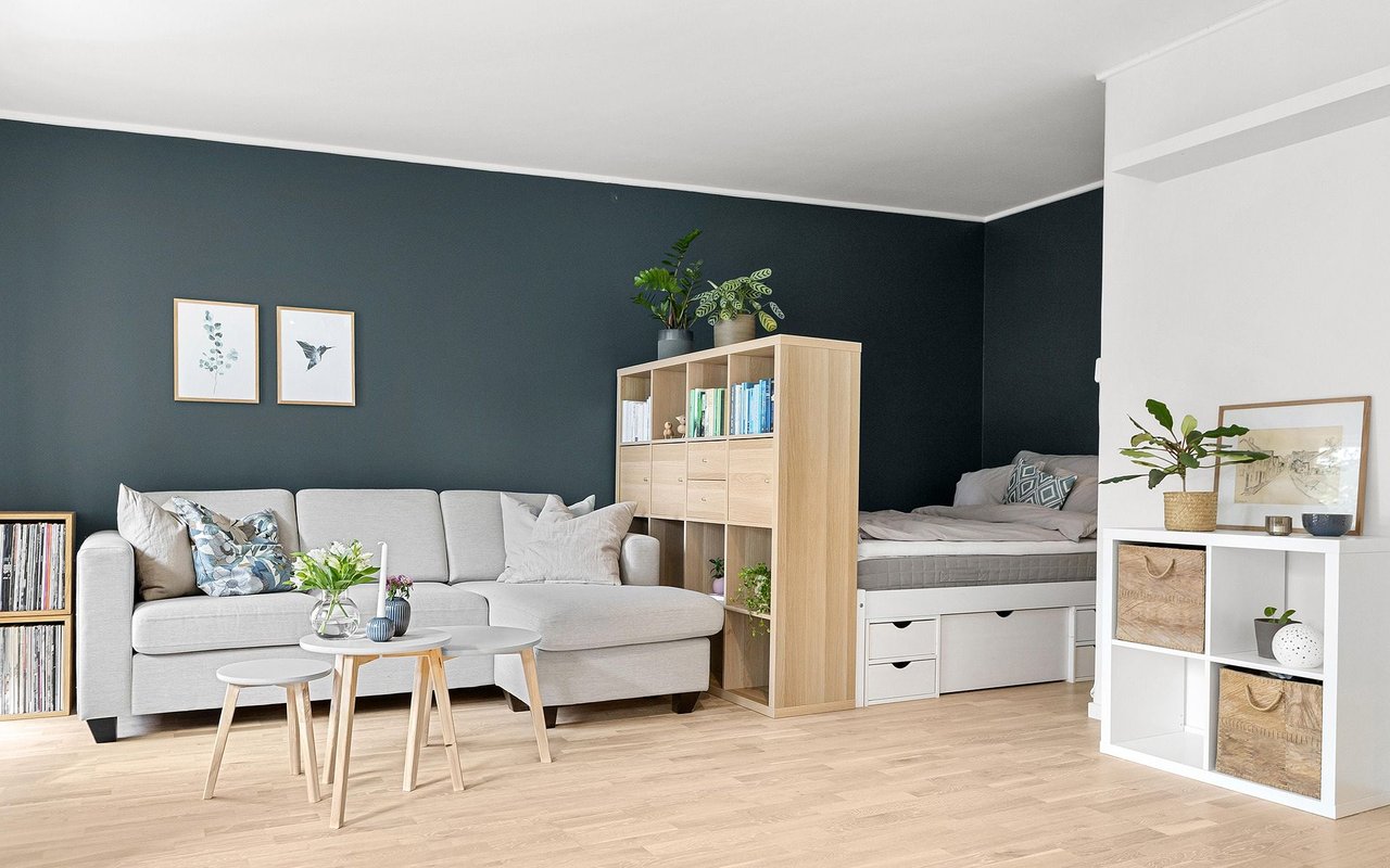 Living room with a gray sectional, dark teal walls, and a sleeping nook behind a bookcase divider.