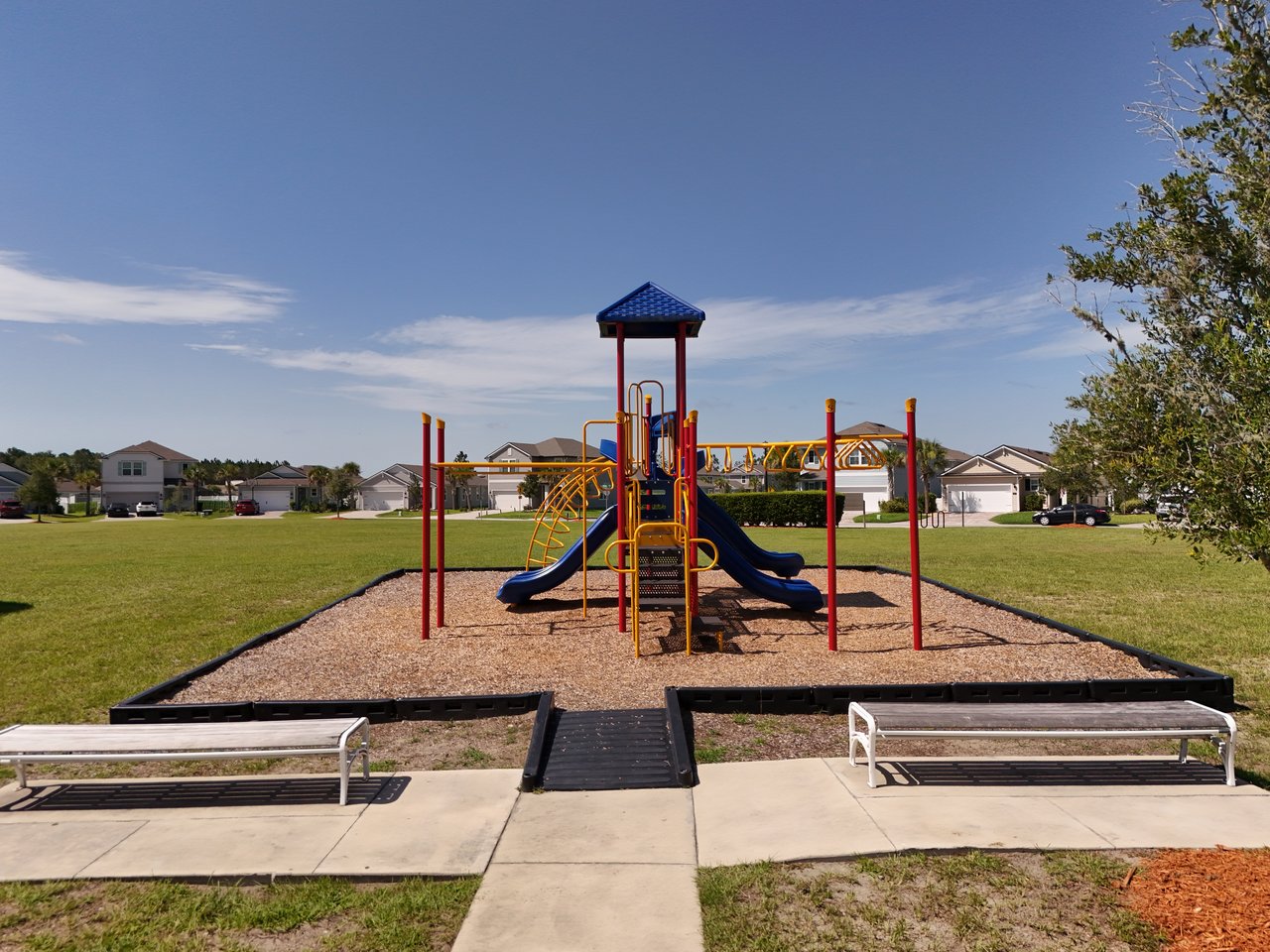 Neighborhood playground with colorful slides, two benches, and houses in the background.