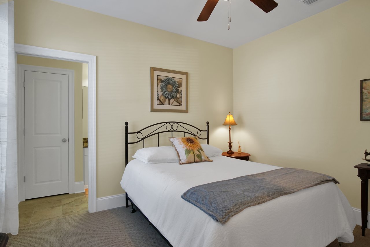 Cozy bedroom with cream walls features a metal bed, sunflower-themed pillow and artwork, side table with lamp, and a closed white door.