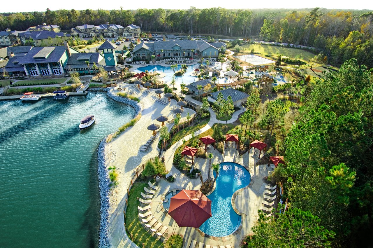 Aerial view of a waterfront community with a clubhouse, pools, sandy shore, and tennis courts.
